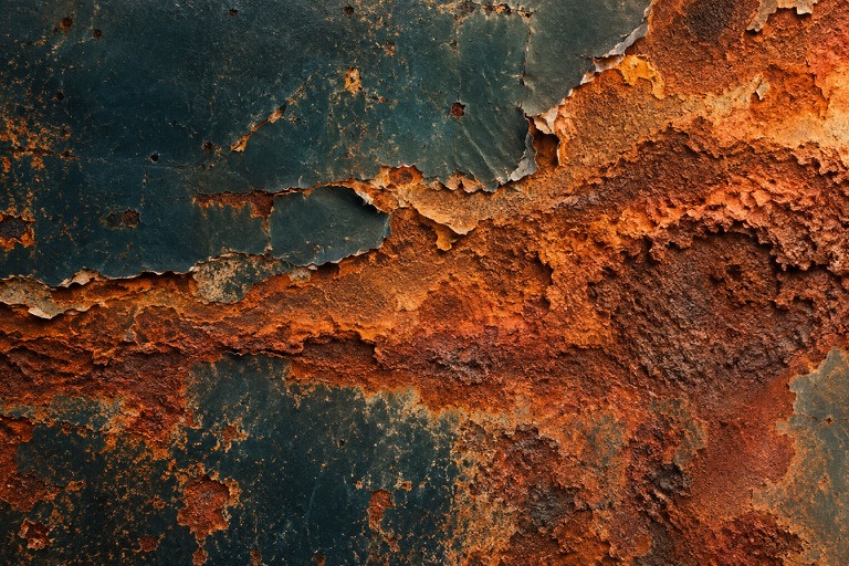 Artistic close view of a reddish rusting iron surface beneath a flaking dark coating